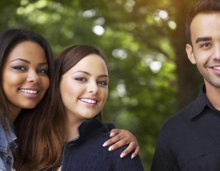 Trois jeunes adultes souriants, en pleine nature, entourés d'arbres.