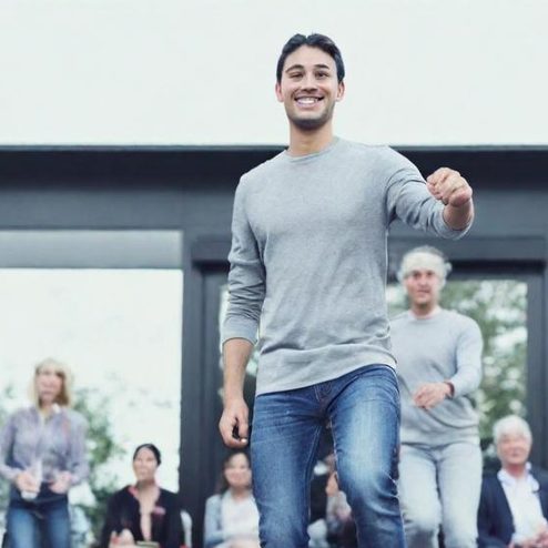 Jeune homme souriant marchant devant un groupe de personnes en arrière-plan.