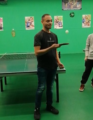 Un joueur de ping-pong tient une balle dans une salle aux murs verts.