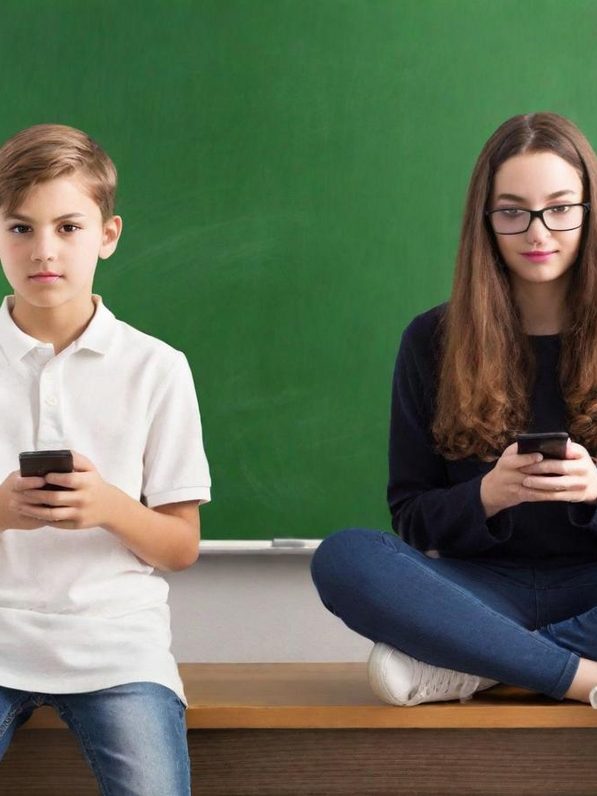 Deux adolescents, un garçon et une fille, consultent leur téléphone près d'un tableau vert.