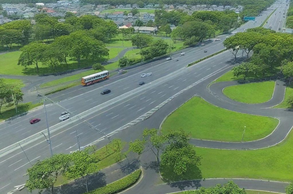 Vue aérienne d'une route avec un bus, entourée de verdure et de zones urbaines.