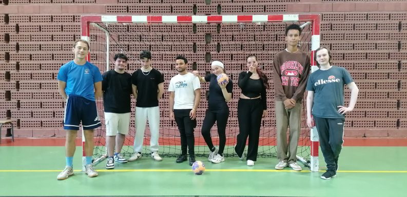 Un groupe de personnes se tenant devant un but de handball dans une salle de sport.