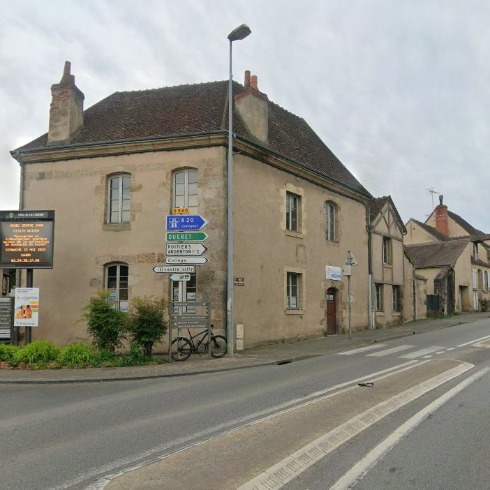 Maison en pierre à l'angle d'une rue, panneaux directionnels à proximité.