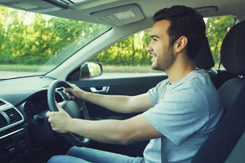 Homme souriant conduit une voiture sur une route ensoleillée.
