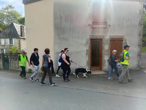 Groupe de personnes marchant le long d'un bâtiment, avec un chien en laisse.