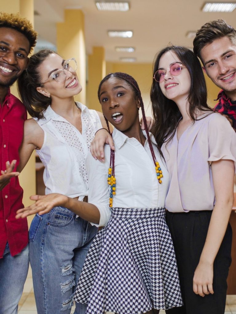 Cinq jeunes souriants posent ensemble dans un intérieur lumineux.