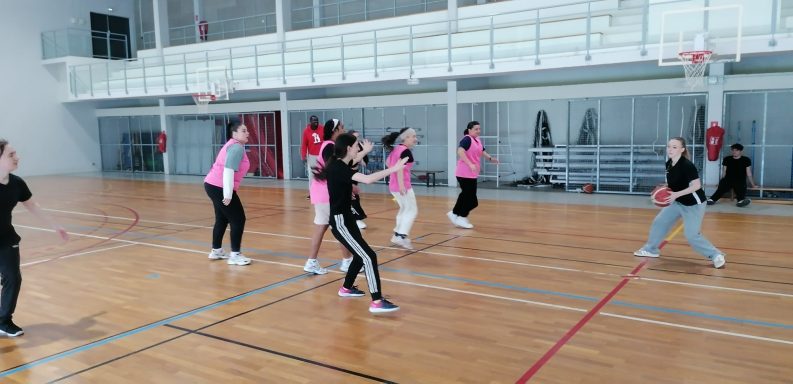 Des femmes en tee-shirts roses jouent au basket dans un gymnase.