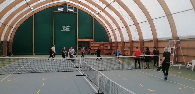 Salle de sport intérieure avec des personnes jouant au tennis sur plusieurs courts.