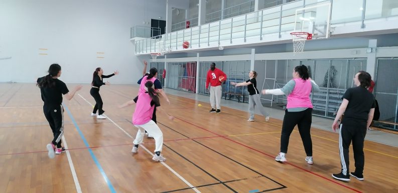 Groupe de personnes jouant au basket dans une salle de sport, portant des maillots roses.