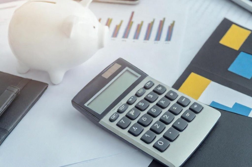 Calculatrice et tirelire sur un bureau avec des graphiques et des documents.