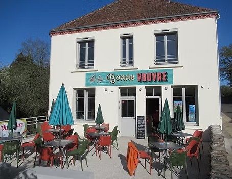 Bâtiment lumineux avec une enseigne, terrasses et parasols colorés.