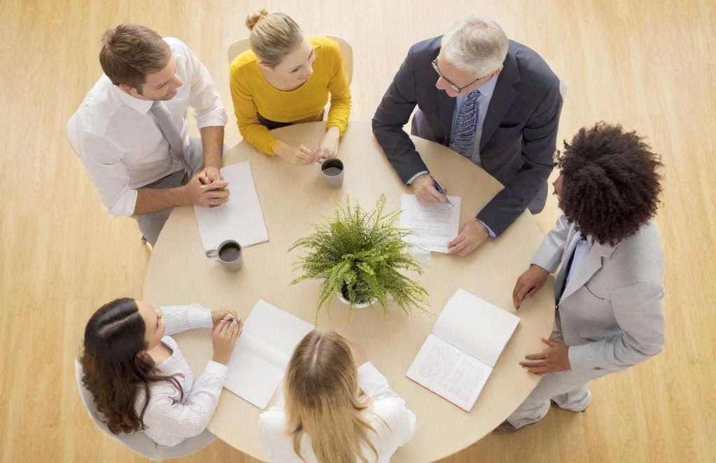 Groupe de six personnes autour d'une table, discutant avec des documents et un plante.