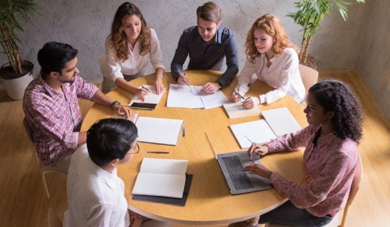 Groupe de personnes en réunion autour d'une table, discutant et prenant des notes.