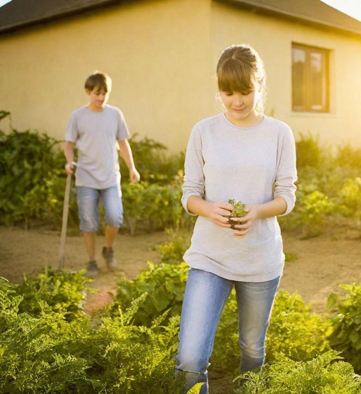 Deux personnes dans un jardin, l'une plante et l'autre désherbe près d'une maison.