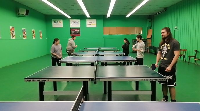 Salle de ping-pong avec plusieurs tables et des personnes se préparant à jouer.