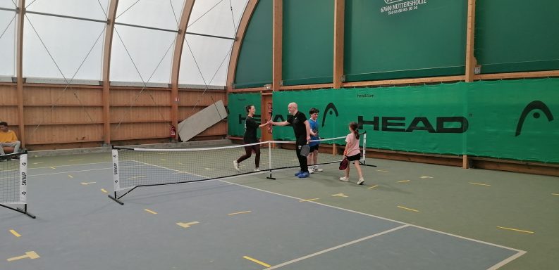 Des enfants jouent au tennis dans un gymnase, passant près du filet.