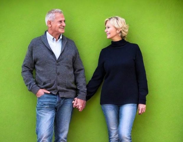 Deux personnes âgées se tenant par la main devant un mur vert.